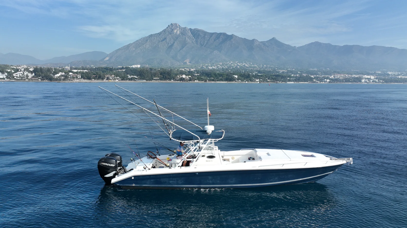 Drone view of STRIKE 360 on blue water off Marbella, with La Concha and the coastline behind